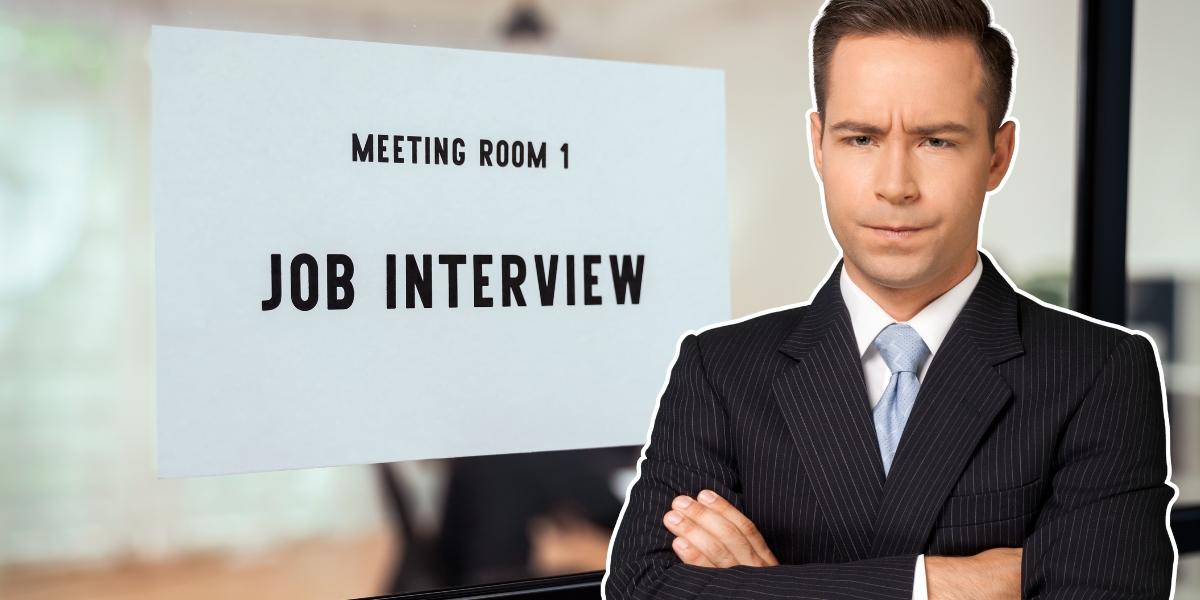 Man i mörkblå randig kostym med armarna i kors står framför skylt med texten "Meeting Room 1 Job Interview"