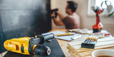 Borrmaskiner och kalkylator på bord med person som renoverar i bakgrunden